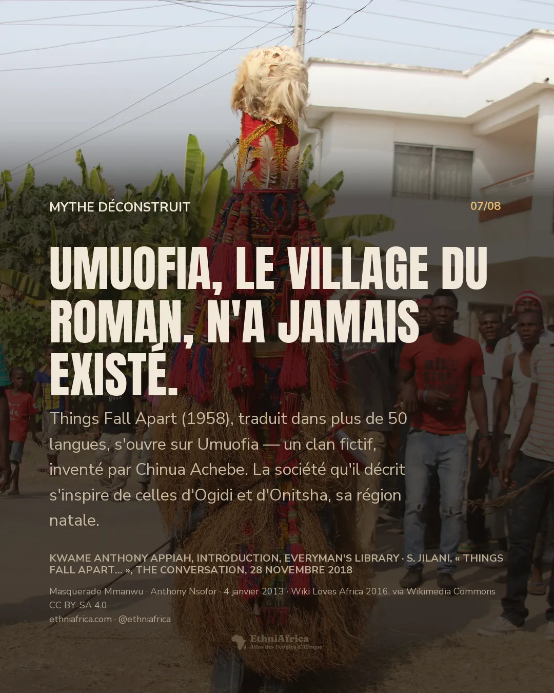 une haute figure de masquerade vêtue de jupes de raphia et de pompons rouges, coiffée d'une toison claire, défile dans une rue résidentielle devant une foule de jeunes gens