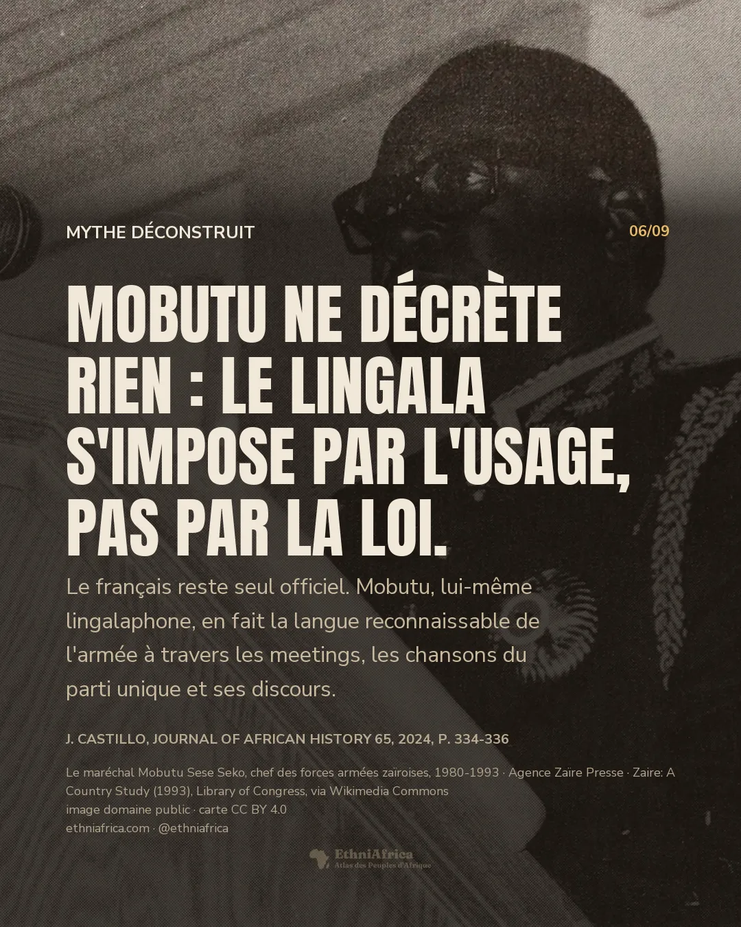 Portrait en légère contre-plongée d'un homme à lunettes, en veste sombre à épaulettes torsadées et décorée d'une médaille, derrière un pupitre équipé de plusieurs microphones.